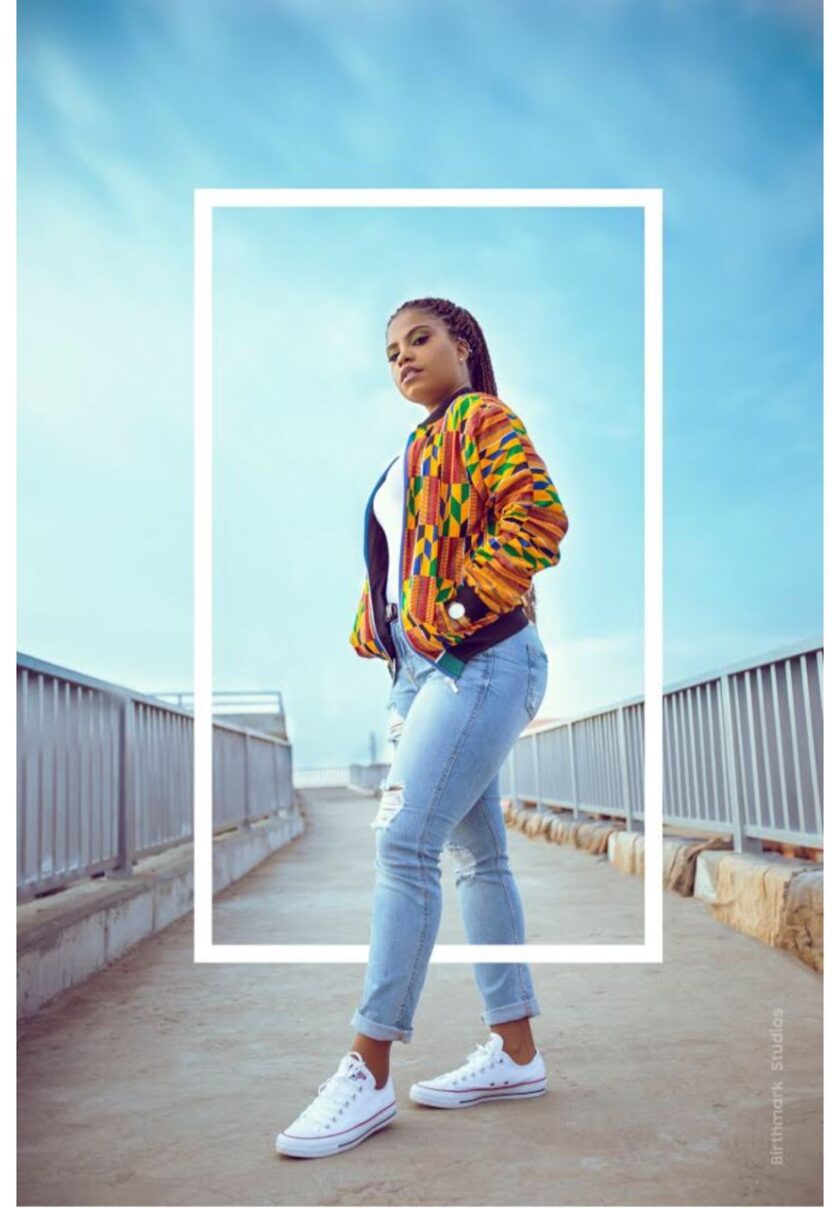 Frontal of model wearing our ladies Deja African inspired bomber jacket in all over vibrant multi-coloured African Kente print pattern. Features a black baseball collar.