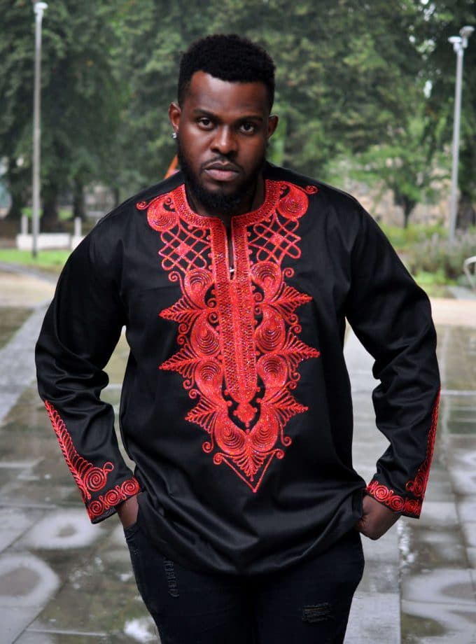 Frontal of model wearing a men's black African shirt with intricate royal style red embroidery on the chest, neckline and cuffs.