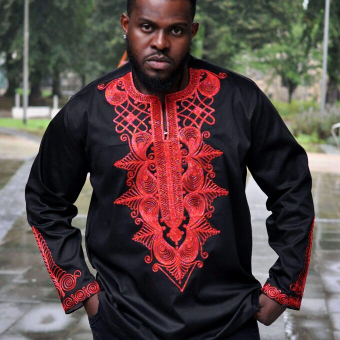 Frontal of model wearing a men's black African shirt with intricate royal style red embroidery on the chest, neckline and cuffs.