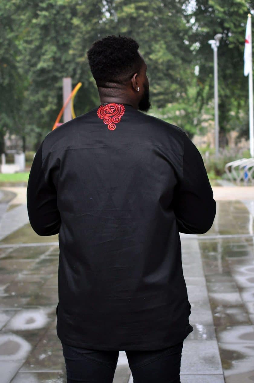 Back shot of model wearing a men's black African shirt with red embroidery on the rear neckline.