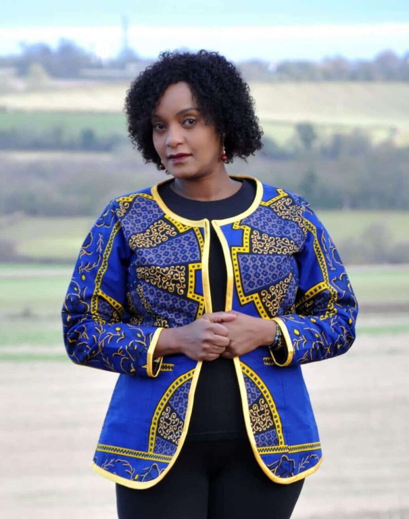 Frontal of model wearing a ladies blue and gold open front jacket in all over African Akufo print.