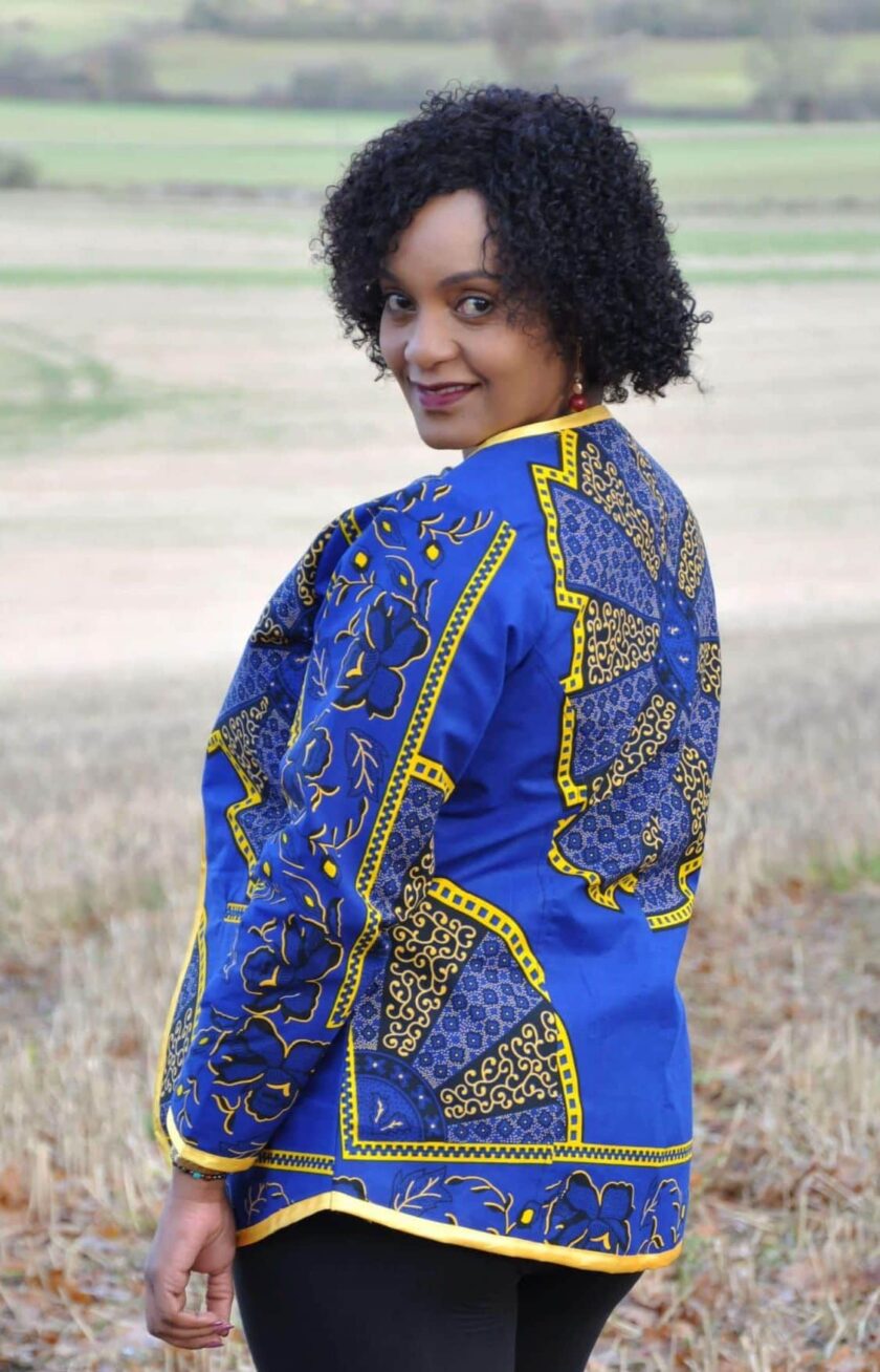 Back shot of model wearing a ladies blue and gold open front jacket in all over African Akufo print.