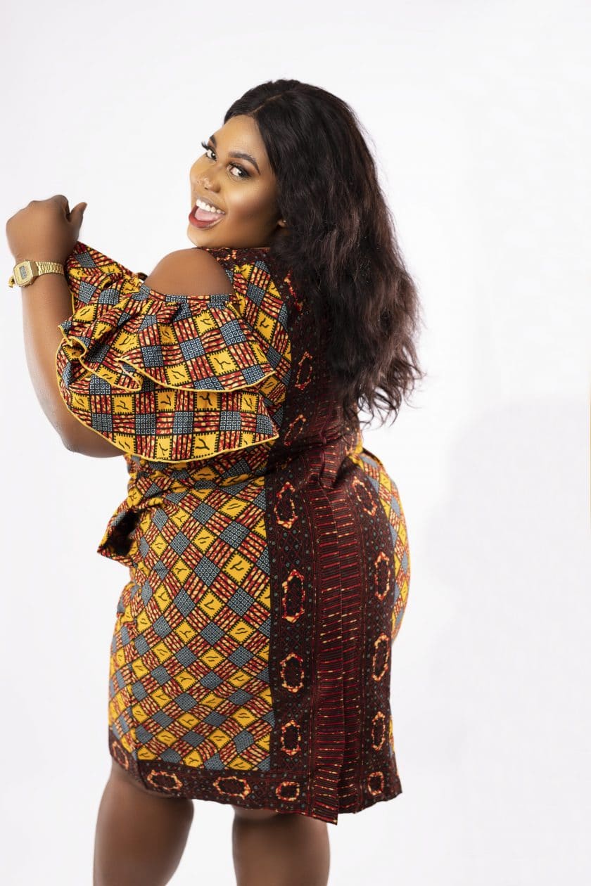 Back shot of model wearing a plus size cold shoulder frill dress in all over African print.