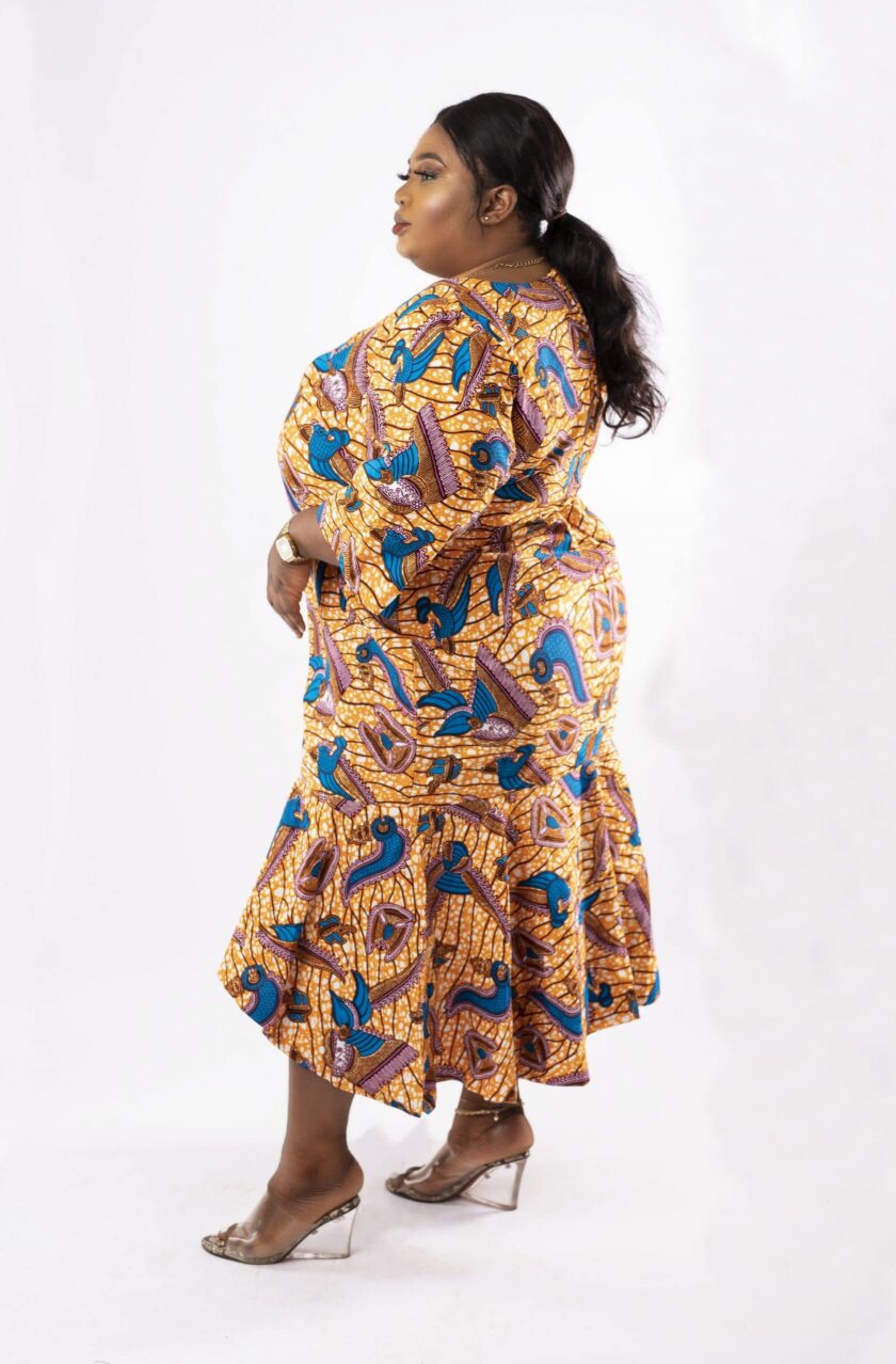 Side shot of model wearing a plus size high low flared midi dress in gold and blue all over African Ankara print.