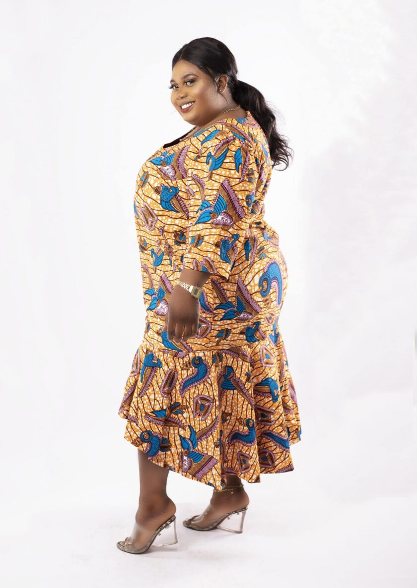 Side shot of model wearing a plus size high low flared midi dress in gold and blue all over African Ankara print.