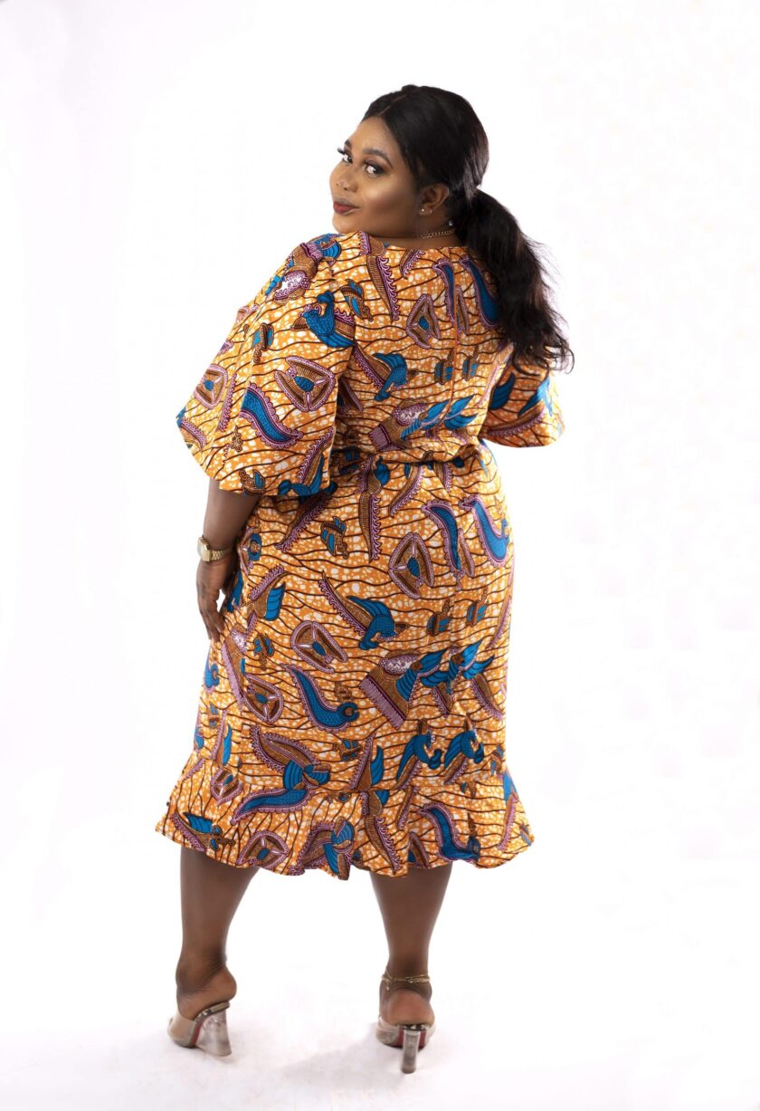 Back shot of model wearing a plus size gold and blue midi dress in all over African print.