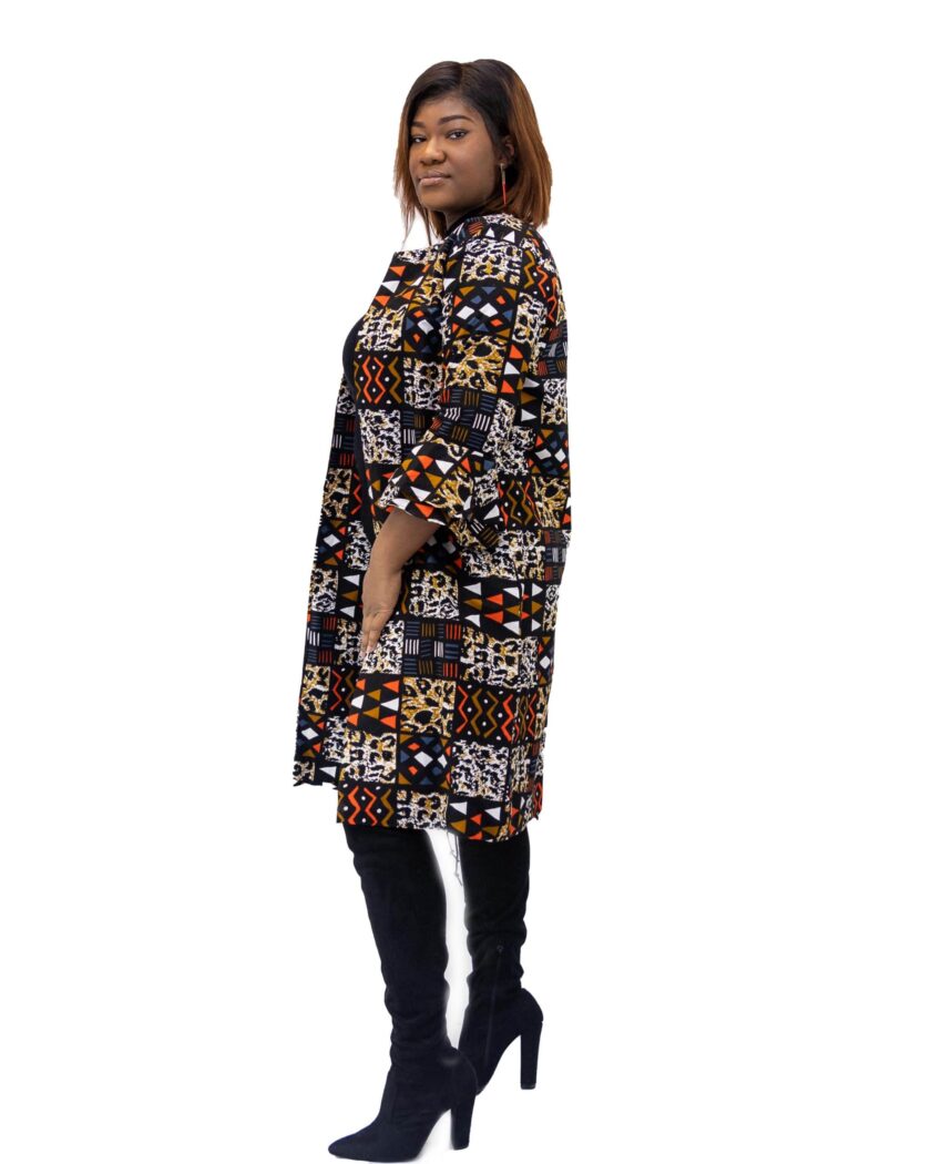 Side shot of model wearing a midi length ladies coat with round neck and all over African patchwork print in orange blue and multi-coloured.