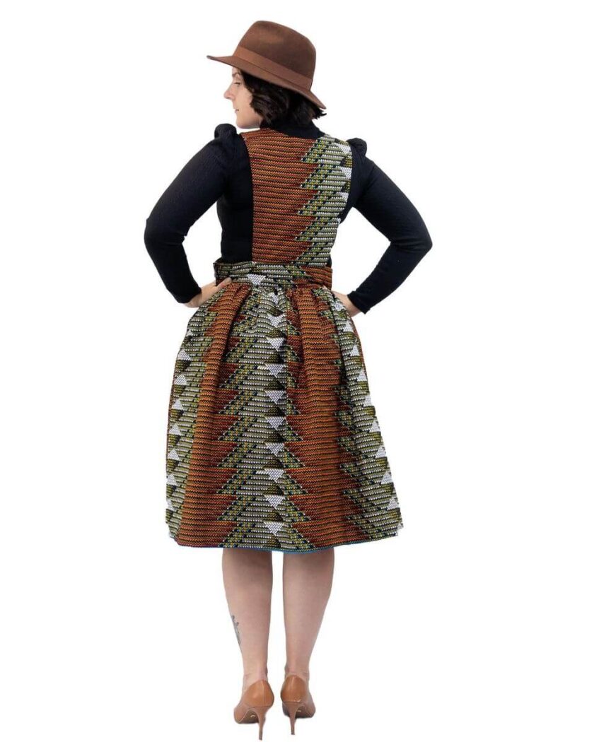 Back shot of model wearing a knee length pinafore skater dress in all over brown and grey geometric African print.