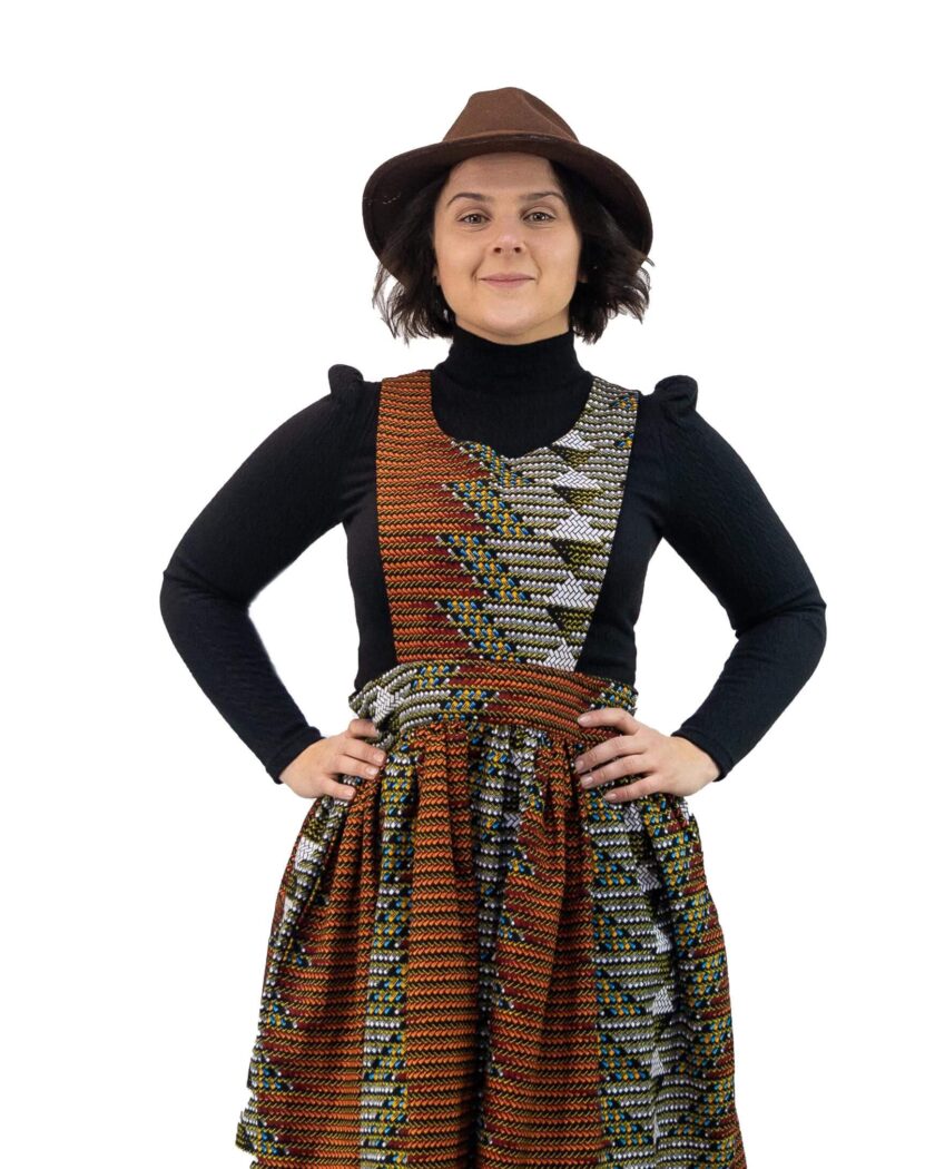 Frontal of model wearing a pinafore skater dress in all over brown and grey geometric African print.
