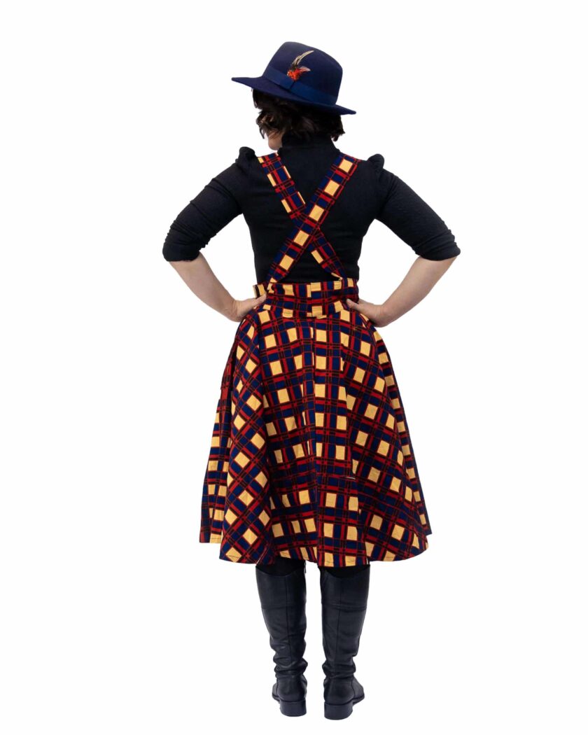 Back shot of model wearing a pinafore dress in all over red, blue and beige African plaid print pattern.