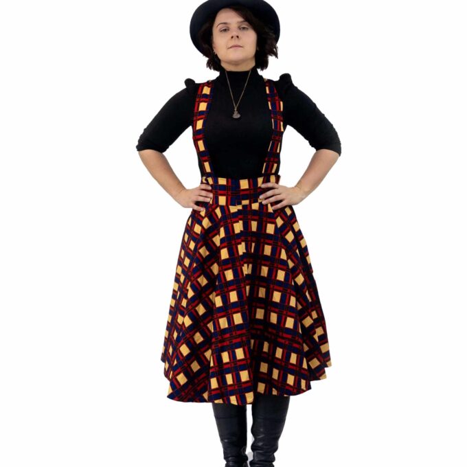 Frontal of model wearing a pinafore dress in all over red, blue and beige African plaid print pattern.