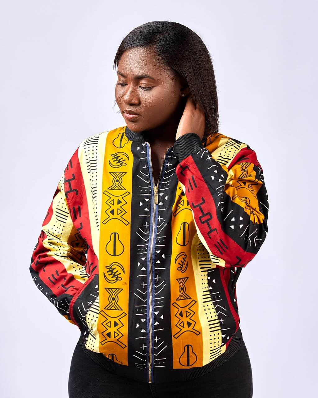 Frontal of model wearing a colourful, striped, ladies bomber jacket in all over African Kente print pattern.