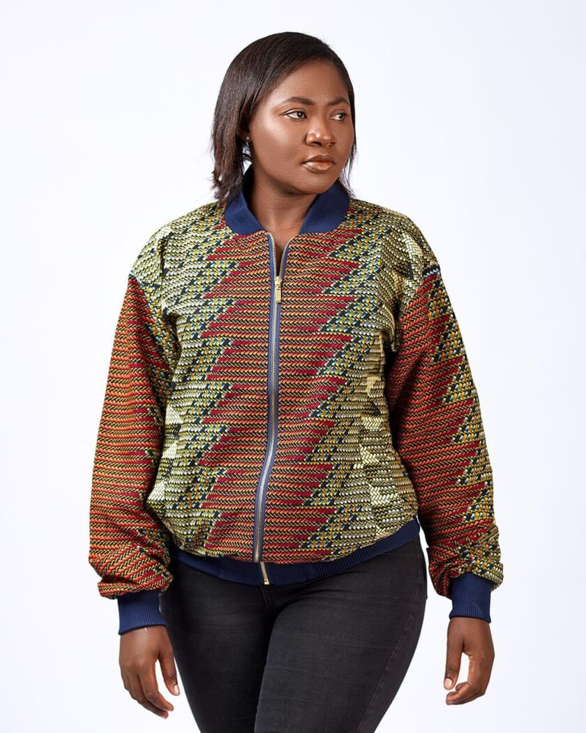Frontal of model wearing a ladies bomber jacket with navy blue baseball collar in all over brown and green graphic African print.