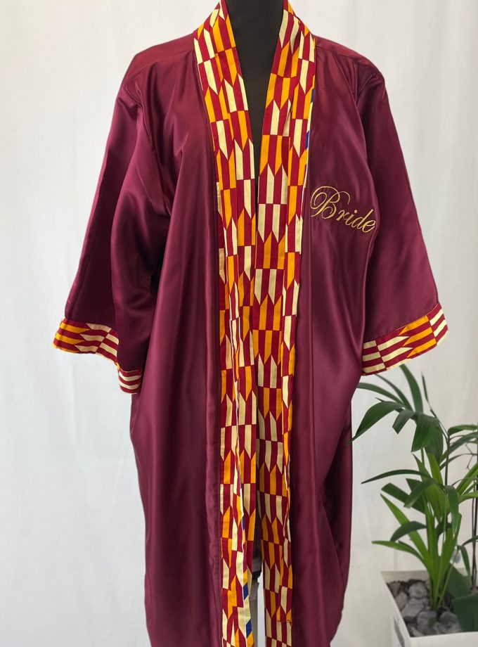 Front shot of a maroon satin robe with the word "Bride" on the front and colourful African print on the sleeve cuffs, neckline and opening.