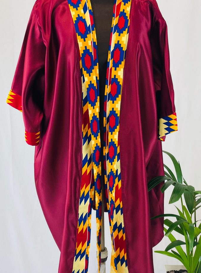 Front shot of a maroon satin robe with colourful African print on the sleeve cuffs, neckline and opening.