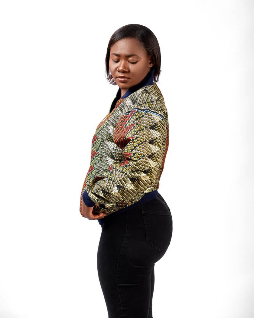 Side shot of model wearing a ladies bomber jacket in all over brown and green graphic African print.
