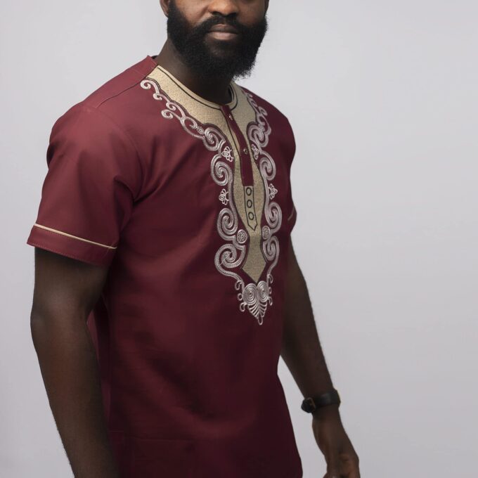 Side shot of model wearing our Muenda Slim Fit Embroidered African Shirt in burgundy / deep red / wine with cream and light pink elaborate embroidery pattern on the neckline, chest and sleeves.