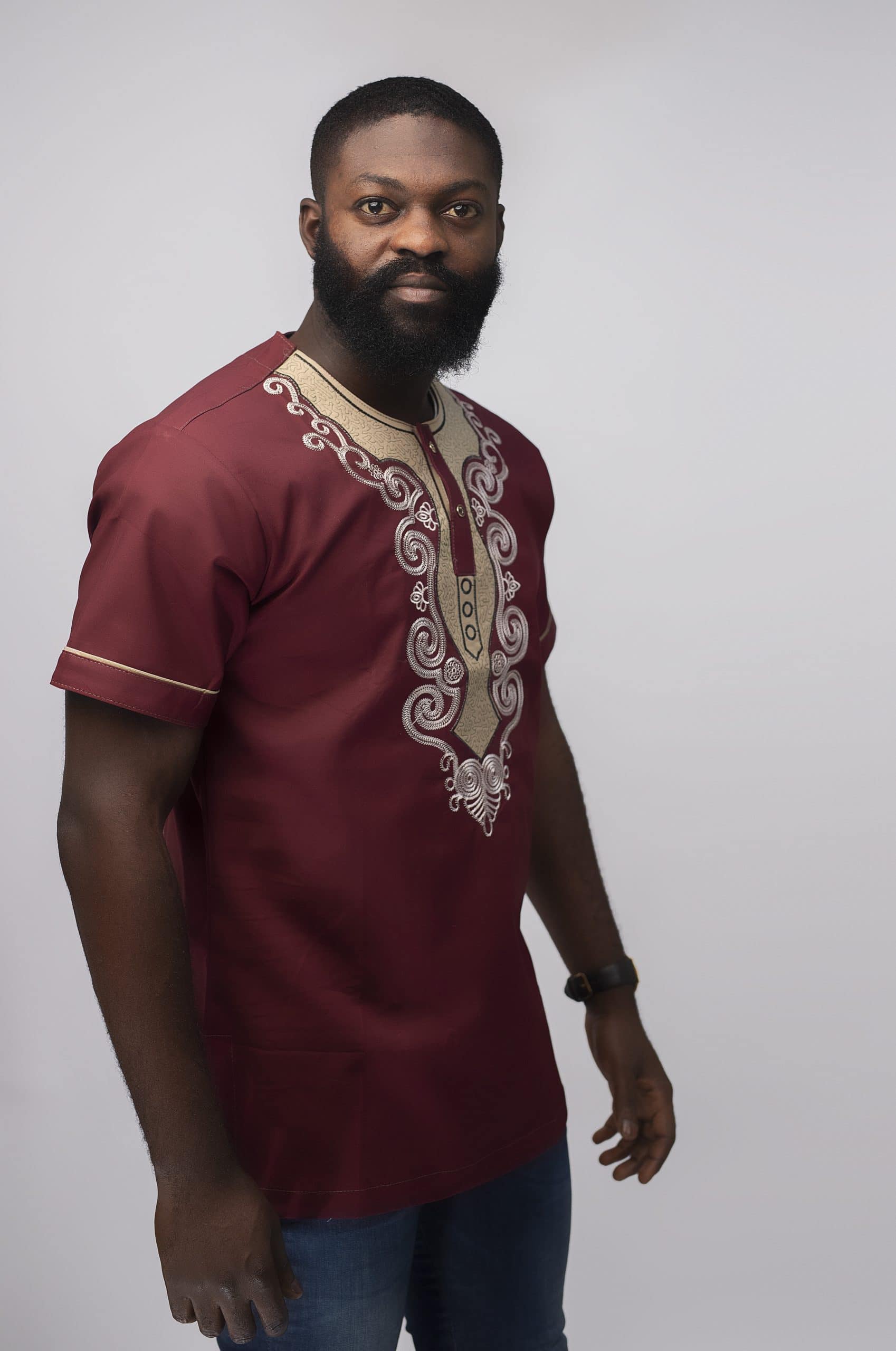 Side shot of model wearing our Muenda Slim Fit Embroidered African Shirt in burgundy / deep red / wine with cream and light pink elaborate embroidery pattern on the neckline, chest and sleeves.