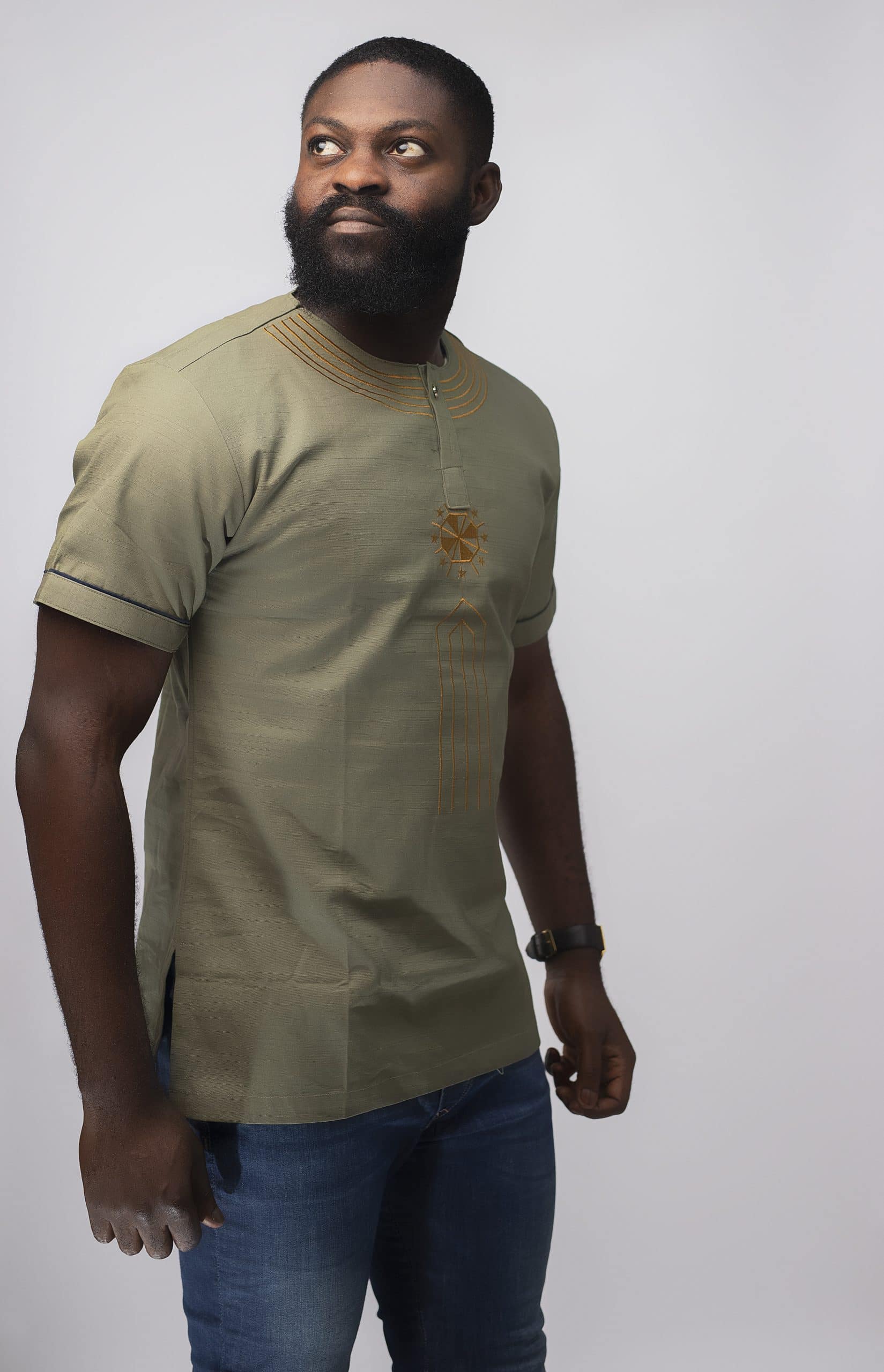 Side shot of model wearing our Momar Slim Fit Embroidered African Shirt in khaki featuring a simple gold embroidery pattern on neckline, chest and black embroidery on the sleeves.
