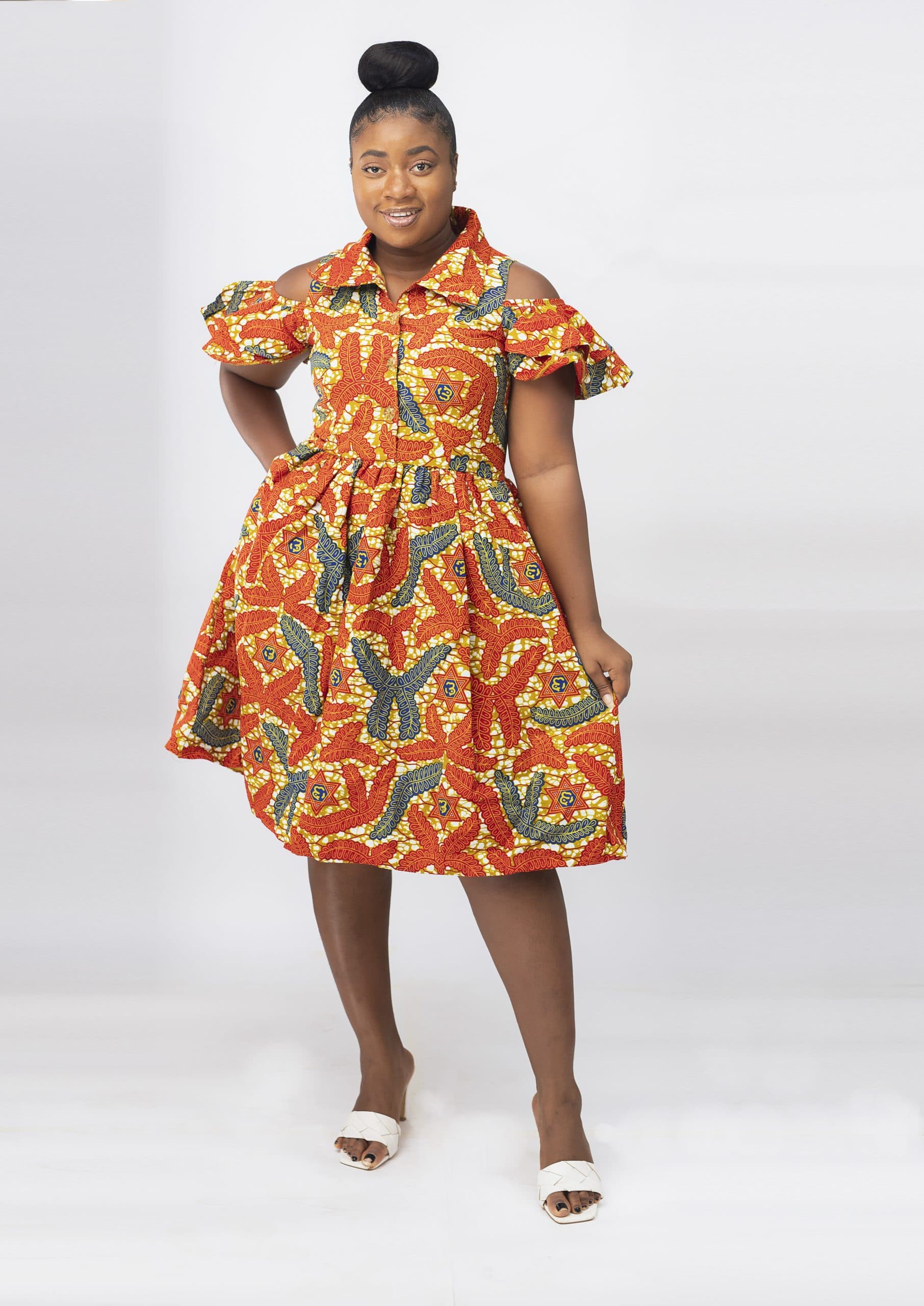 Frontal of model wearing our Oluchi skater midi dress in all over orange, gold and blue African print pattern. Features a cold shoulder, short sleeve, collar neckline.