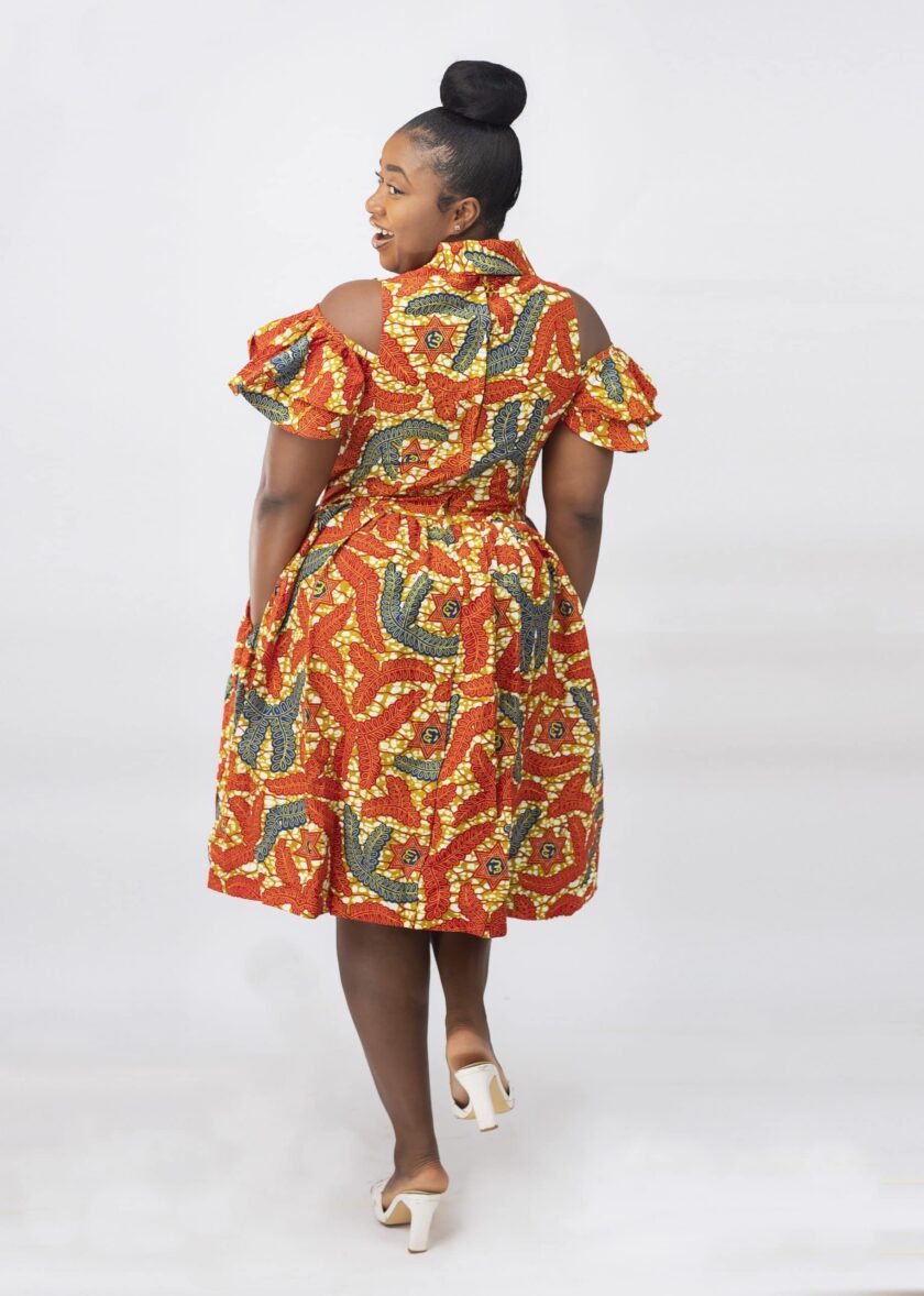 Back shot of model wearing our Oluchi skater midi dress in all over orange, gold and blue African print pattern. Features a cold shoulder, short sleeve, collar neckline.