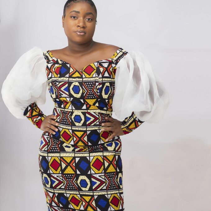 Full frontal of model wearing an elegant bodycon dress with all over colourful African print. Features balloon sleeves in white illusion mesh material.