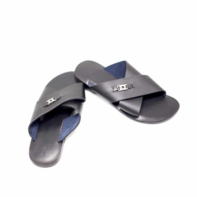 Shot of men's black leather slide sandals with cross strap design and metal decor detail.