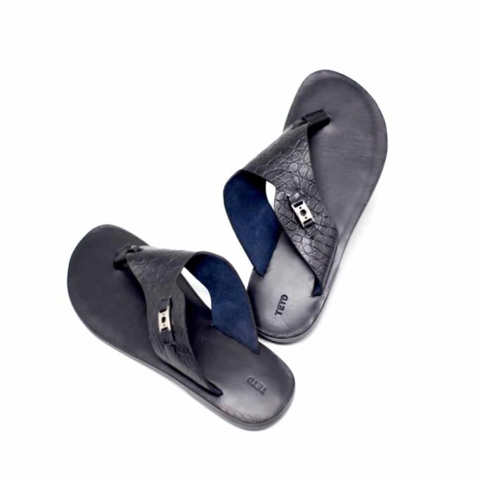 Shot of men's black leather flip flop sandals with metal decor and crocodile pattern.