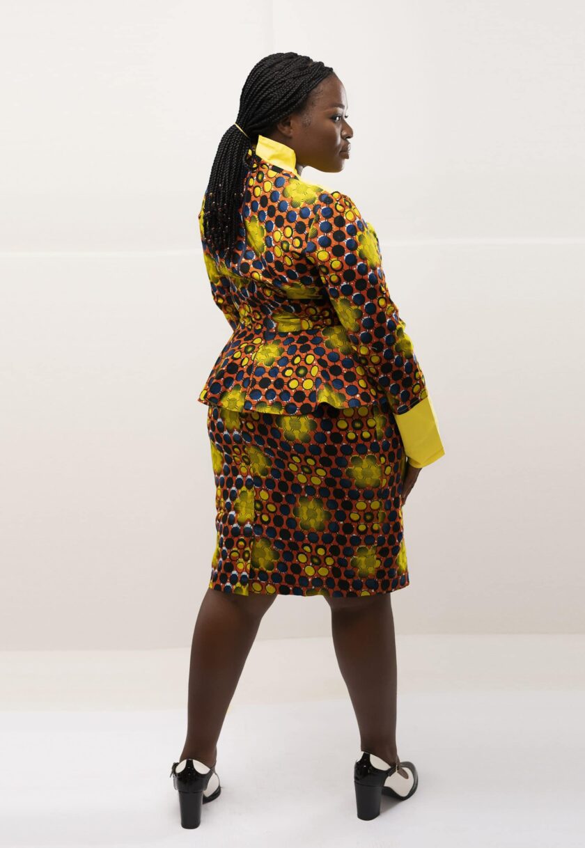 Back shot of model wearing our Zuri two piece matching peplum skirt set in yellow, brown and blue African print. Features a statement collar and contrasting solid yellow panel on front and cuffs.