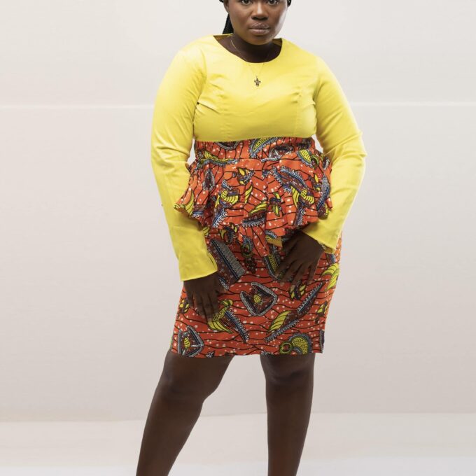 Frontal of model wearing our Haniah two piece top and skirt set in solid yellow and contrasting orange Ankara / African print. Features a pencil skirt with peplum ruffle.