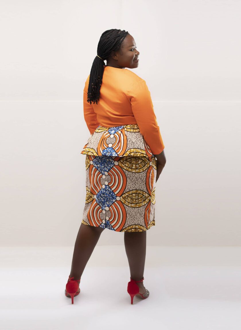 Back shot of model wearing our Amma two-piece skirt set in peach orange tones and multi-coloured African print. Features a peplum top and matching skirt.