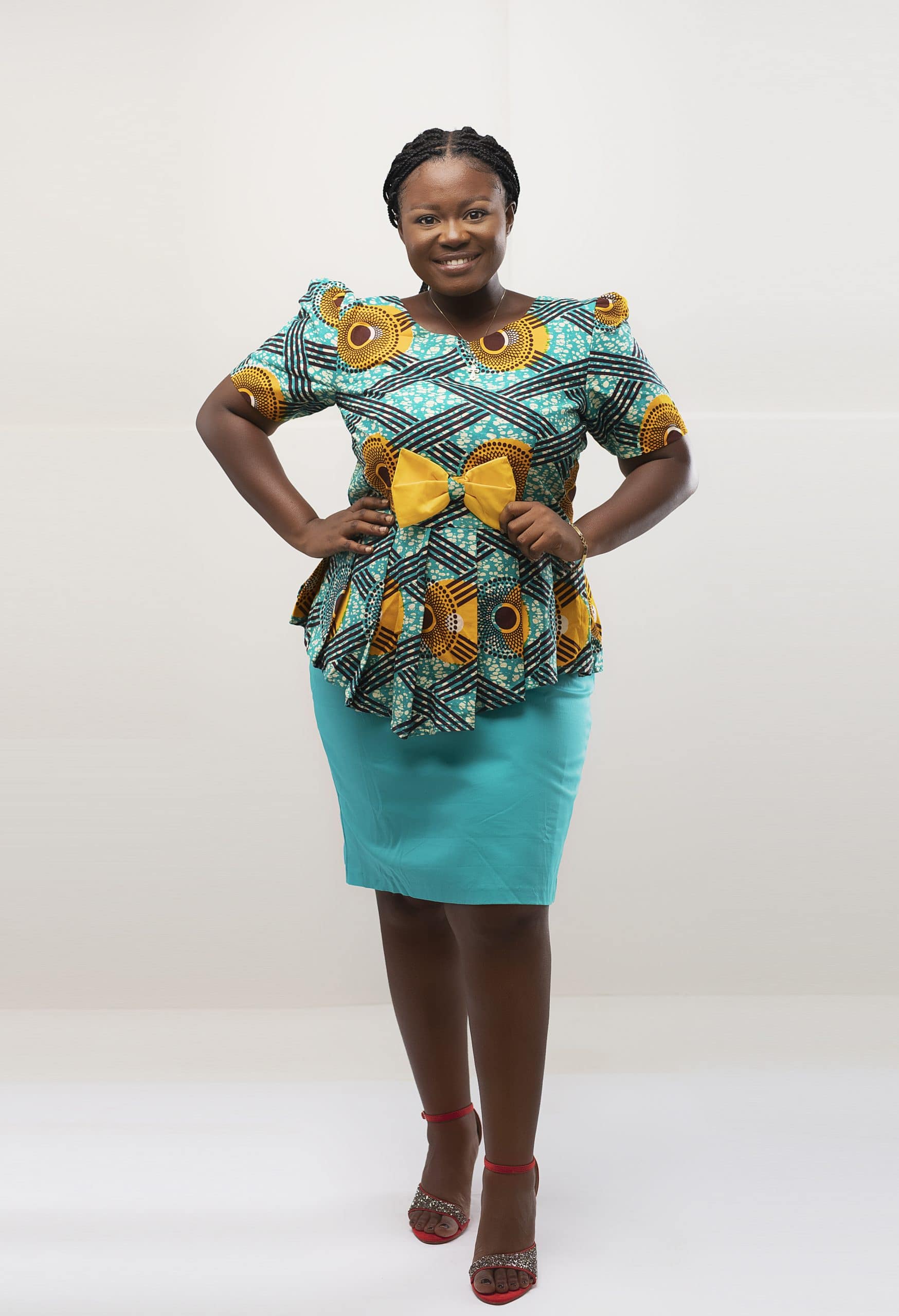 Frontal of model wearing our Abina two piece peplum top and skirt set in light blue and yellow African print. Features a contrasting solid light blue pencil skirt and sash bow.