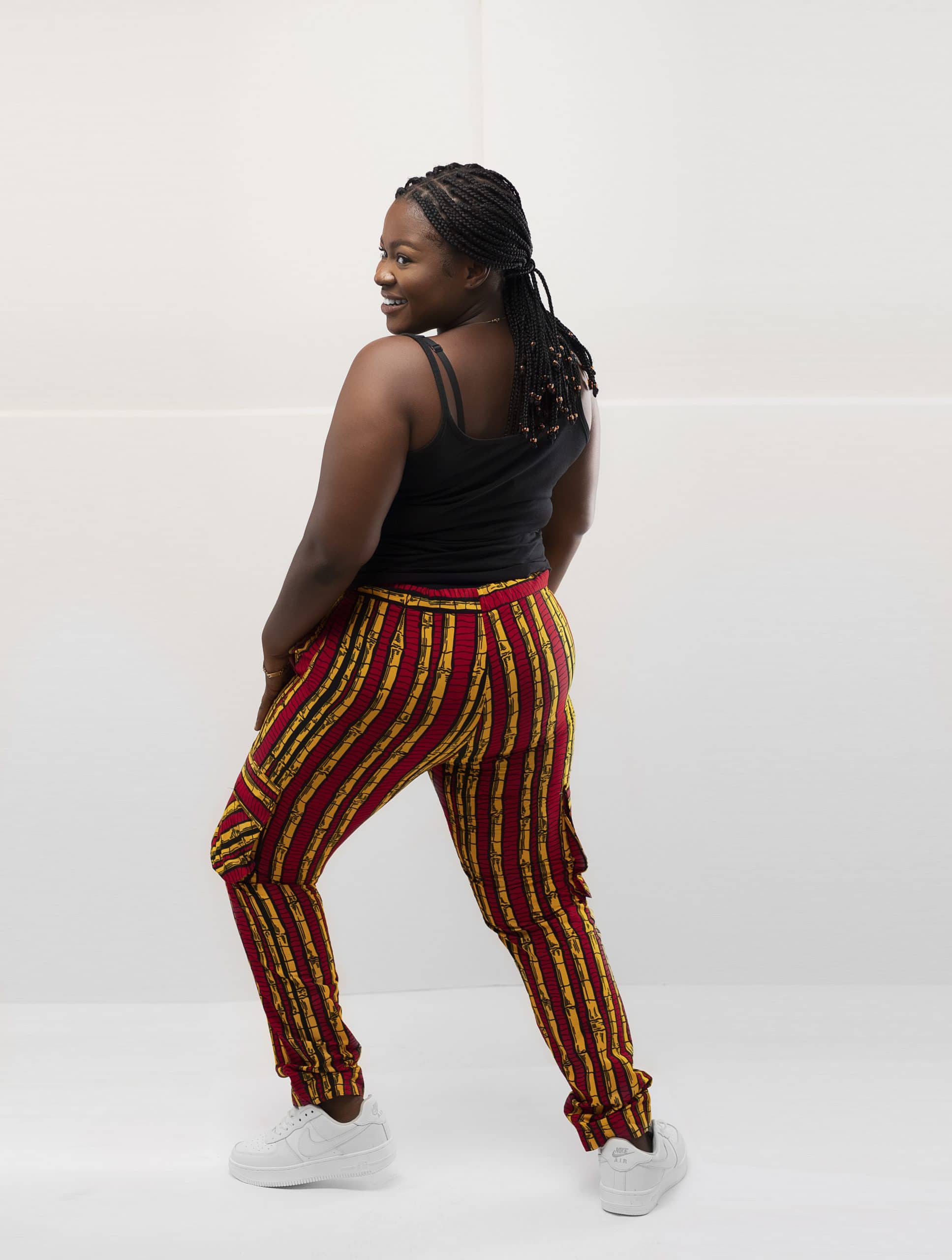 Back shot of model wearing our ladies Shani combat trousers or cargo pants in all over striped red and gold African print.