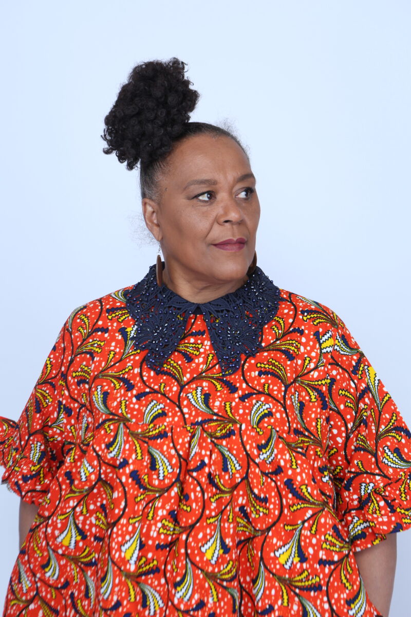 Woman posing while wearing a blue collar orange african print dress