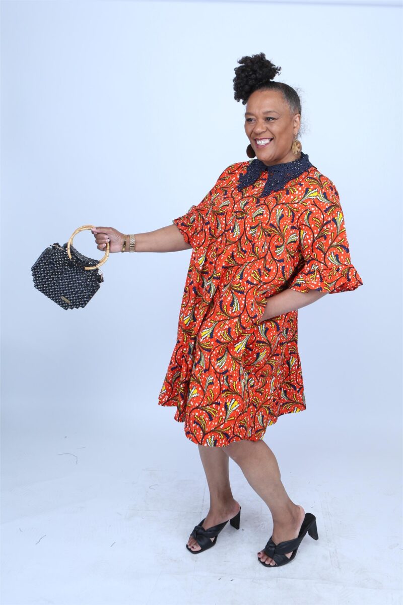 Woman posing while wearing a blue collar orange african print dress